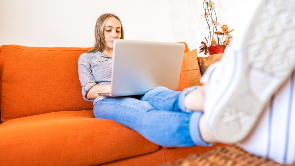 Blonde smart gen z girl using laptop sitting at home sofa to shopping online. Young student enjoying internet to connect at school network and classmates. New normal activity of online remote lessons
