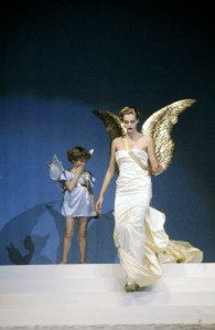 In March 1984 Thierry Mugler celebrated the tenth anniversary of his ready to wear label with the first commerical runway show. Presented to a paying audience of six thousand people at the Zenith stadium in Paris; in Mugler's larger-than-life production models on the runway participated in themed vignettes centered around Olympian, space-age, and religious themes.