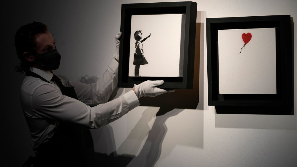A member of staff holds up an artwork by British graffiti artist Banksy entitled 'Girl and Ballon' (two parts), during a pre-auction press viewing at Christie's auction house in London, Friday, Oct. 1, 2021. The diptych is expected to sell for 2,500,000 million pounds sterling (US, $3.5-4.8 million, euros 3-4.1 million). (AP Photo/Alastair Grant)