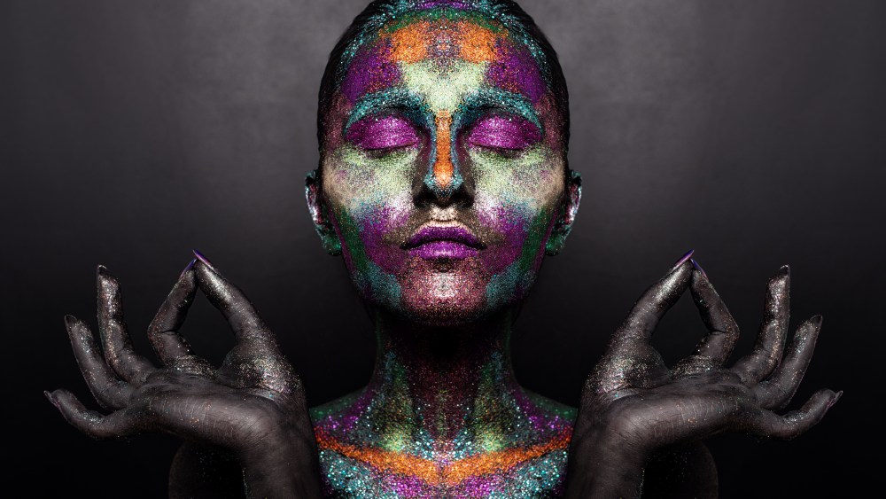 Young artistic woman in black paint and colourful powder. Glowing dark makeup. Creative body art on the theme of space and stars. Bodypainting project: art, beauty, fashion