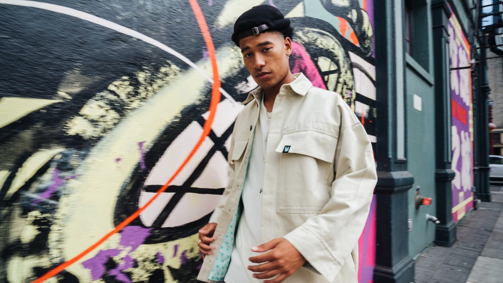 Unless sustainable streetwear brand man wearing canvas jacket in front of street mural