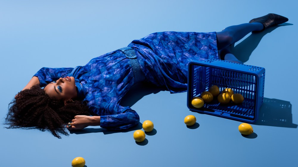 african american woman lying with shopping basket and lemons on blue background