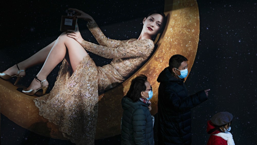 Shoppers wearing face masks to help curb the spread of the coronavirus walk by a Chanel perfume advertisement billboard on display at a capital popular shopping mall in Beijing.