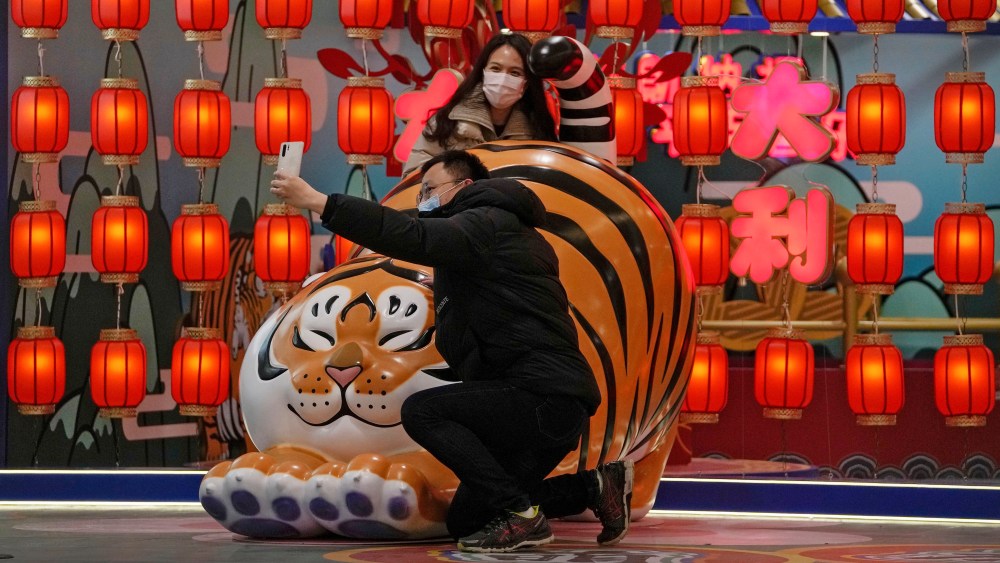 A couple wearing face masks to protect from the coronavirus take a selfie with a tiger decoration at a shopping mall in Beijing