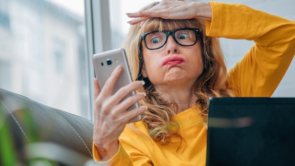 stressed out woman looking at cell phone at home with computer