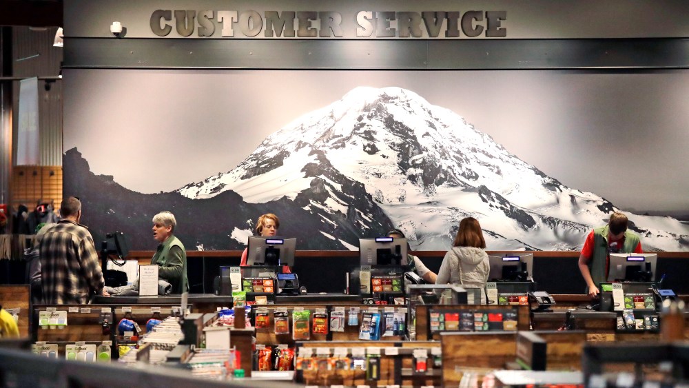 In this photo taken Nov. 13, 2018, clerks work in front of a large photo of Mount Rainier in REI Co-op's flagship store in Seattle. For the fourth consecutive year, REI said that on the popular Black Friday shopping day it will close all 153 stores, process no online payments and pay more than 12,000 employees, encouraging them to recreate outdoors with friends and family. The company calls it #OptOutside. (AP Photo/Elaine Thompson)