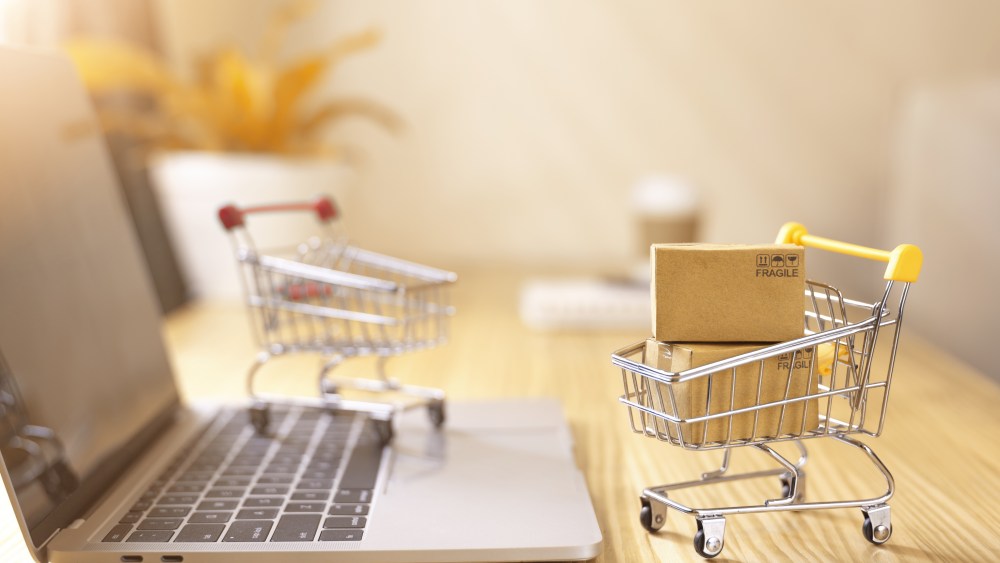 Online shopping and delivery service concept.Brown paper boxs in a shopping cart with laptop keyboard on wood table in office background.Easy shopping with finger tips for consumers.