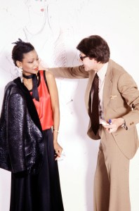 Mounia poses in a look from the Yves Saint Laurent RTW Fall 1978 collection as designer Yves Saint Laurent sketches on wallpaper in his atelier in Paris on March 15, 1978.