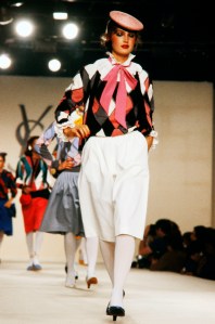 Anne Besamet walks the in a harlequin print jacket and white drindle skirt from the Yves Saint Laurent RTW Spring 1980 collection.