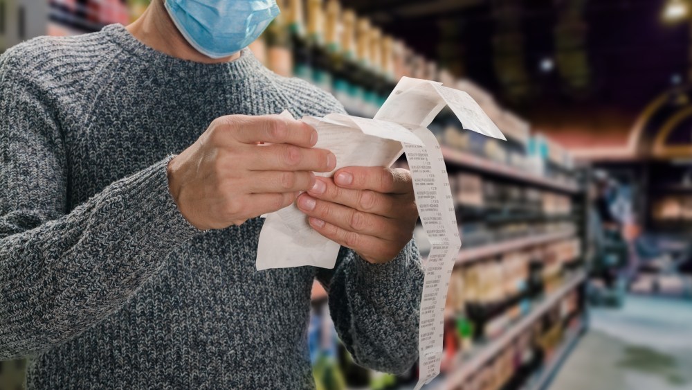 Male customer doing grocery shopping at supermarket and feeling confused by bill