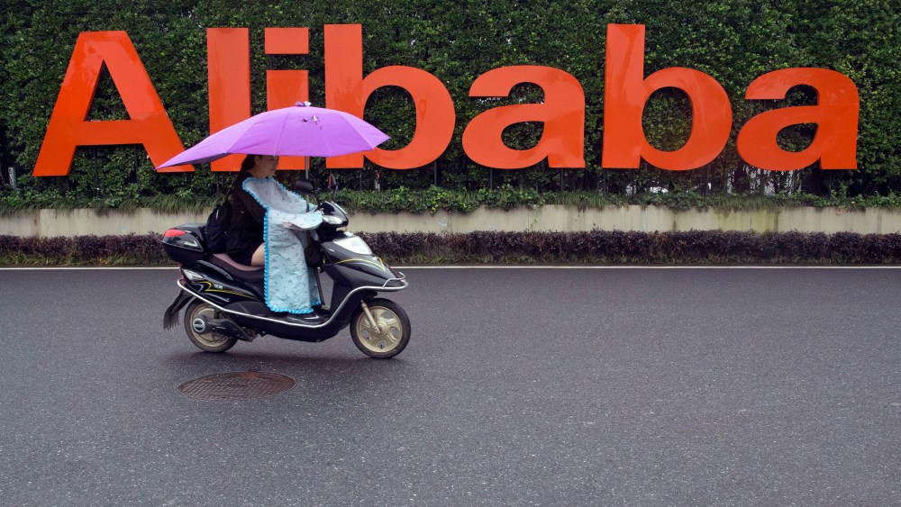 A woman rides a scooter past the company logo outside the Alibaba Group headquarters in Hangzhou.