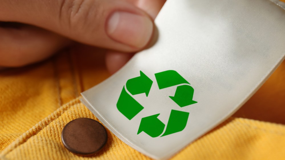 Woman showing clothing label with recycling symbol on yellow jeans, closeup