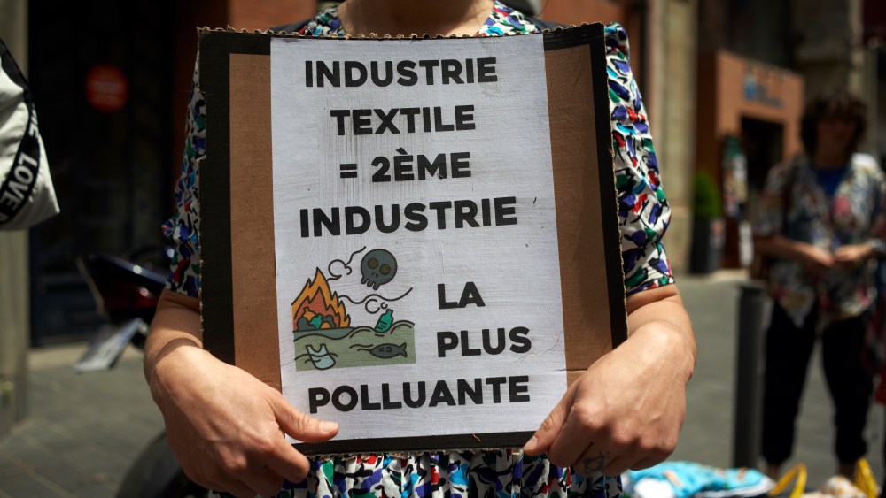 A woman holds a cardboard reading 'Textile industry = 2nd most polluting insdutry'. Members of XR Toulouse (Extinction Rebellion) organized a protest in front of a pop-up SHEIN shop. The chinese brand SHEIN opened a pop-up store in Toulouse only for 4 days. XR wanted to raise awareness about water consumption and waste, over consumption of ressources, workers' conditions and abuse of human rights in China. They are against fast fashion as it's a waste of natural ressources. Toulouse. France. May 28th 2022. (Photo by Alain Pitton/NurPhoto via AP)