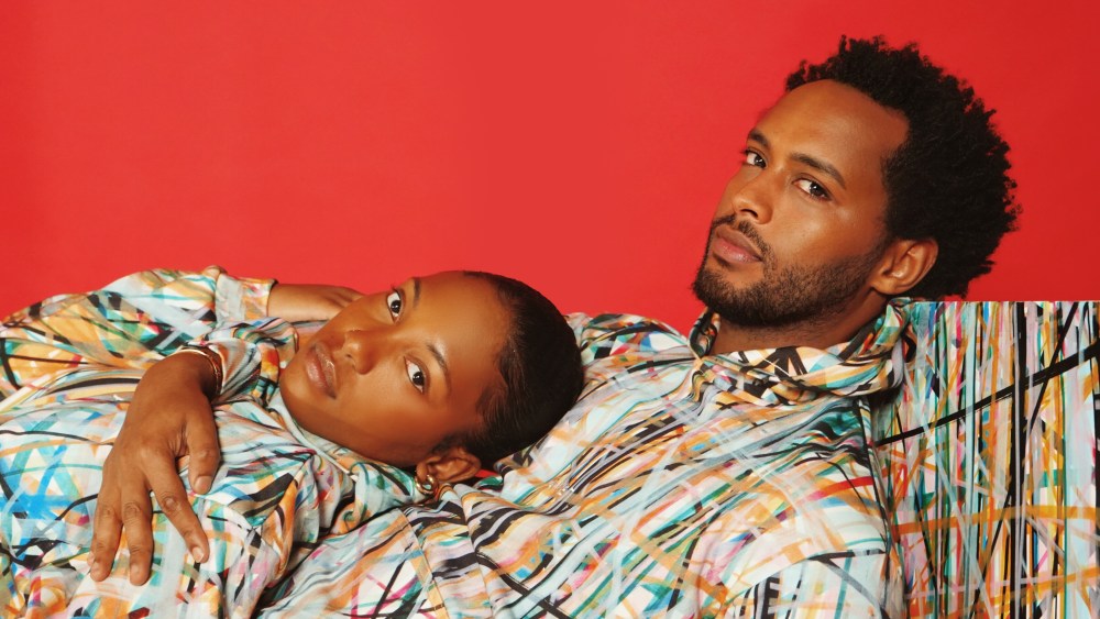 Two Black people laying down wearing Áwet New York's Juneteenth capsule sweatsuit that is designed like a painting strewn with colorful lines