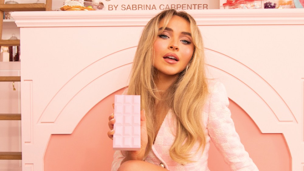 Sabrina Carpenter posing with perfume bottle.