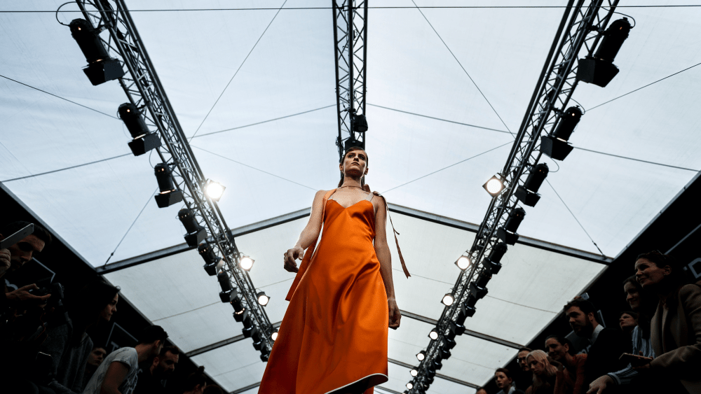 A model walks at Madrid Fashion Week in an orange dress made of majority recycled materials.