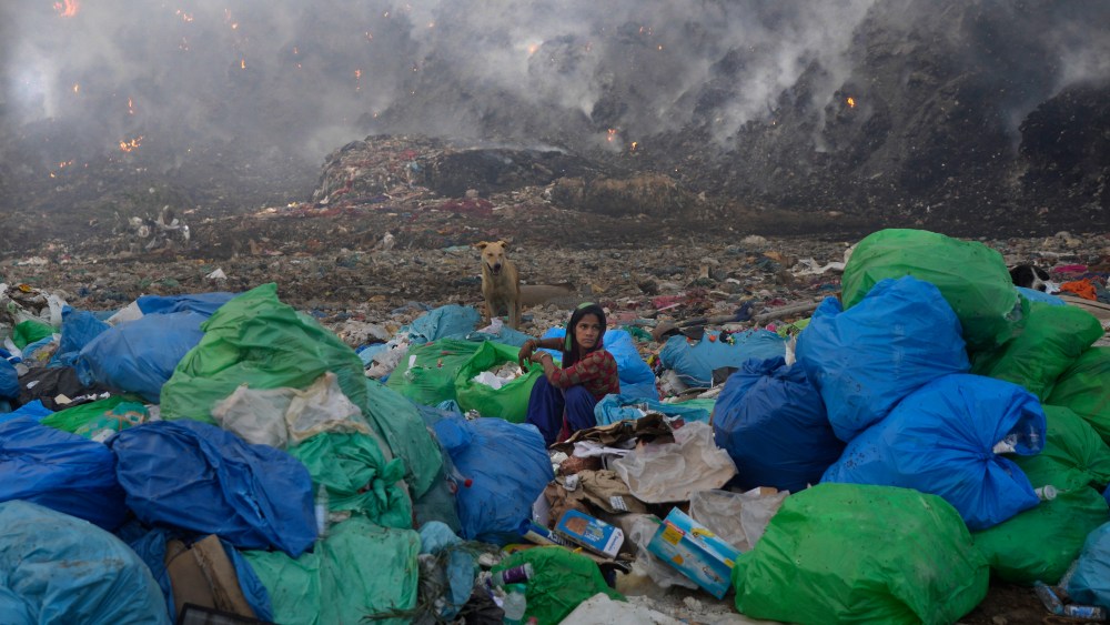 A ragpicker woman segregates items sitting at the edge during a fire at the Bhalswa landfill in New Delhi, India, Wednesday, April 27, 2022. India's capital, which like the rest of South Asia is in the midst of a record-shattering heat wave, was left enveloped in thick acrid smoke. (AP Photo/Manish Swarup)