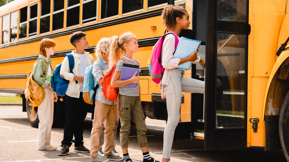 Schoolchildren kids pupils group of mixed-race classmates boarding school bus before going to lessons, coming back to school, standing in line. New educational year semester.