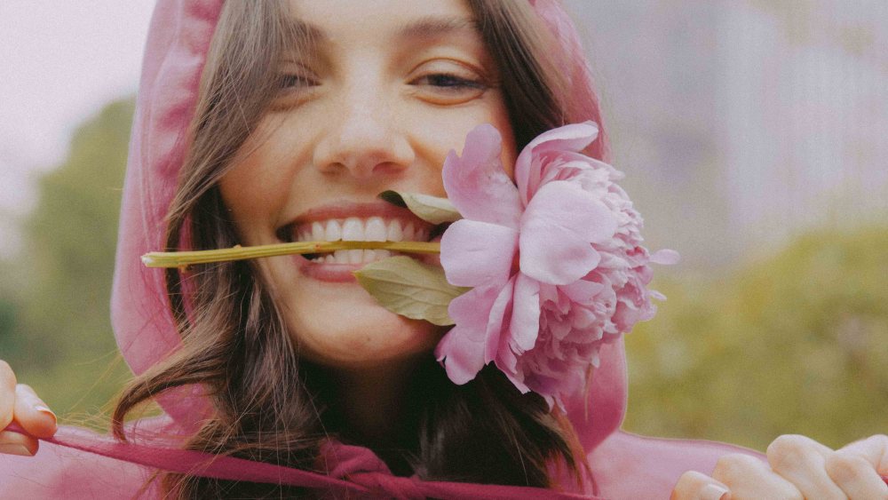 A model clutches a pink flower in her teeth in a foggy morning in Central Park with a Valentino sweatshirt on in a matching hue.