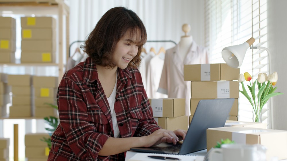 Young asia people woman female e-commerce parcel work check typing talk to customer on notebook for box shipping online fulfillment sme dropshipping digital dispatch app clothes fashion supply chain.