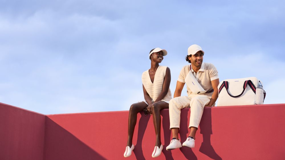 A model couple seated on a red-orange and fuchsia ledge wearing Rothy's visor, sling and tennis racquet.