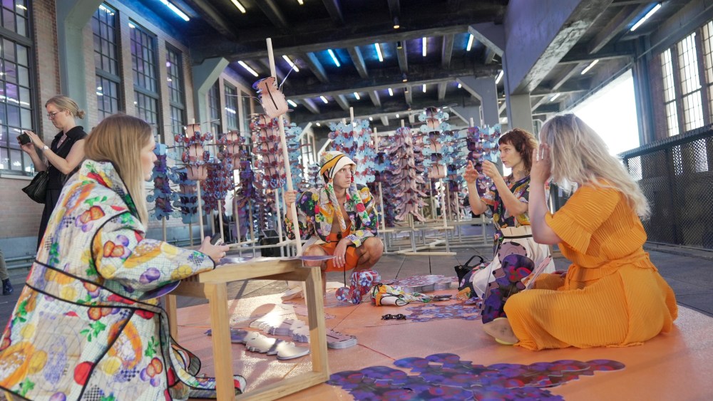 Four people dressed on colorful clothing sit on the floor in the center of Henrik Vibskov's "Jungle of Tongues and Ears" installation.