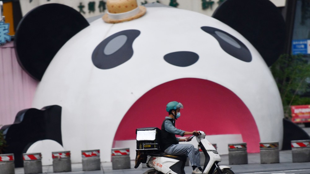 A Meituan food courier rides an electric bike past a giant panda sculpture in Chengdu on September 2, 2022.