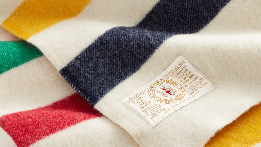 A close-up shot of the Hudson's Bay blanket which is off white with blue, yellow, green and red stripes.