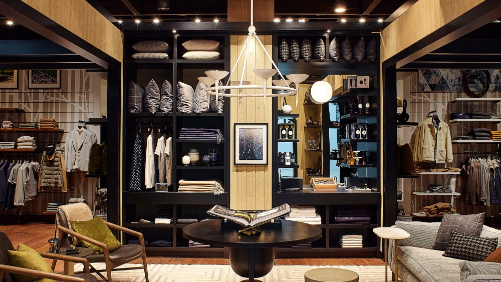 The installation is in Harry Rosen's Yorkdale Centre store in Toronto. features store set up like living room with couch to the right, coffee table at center, two chairs to the left and product on back wall displayed as if in a closet.
