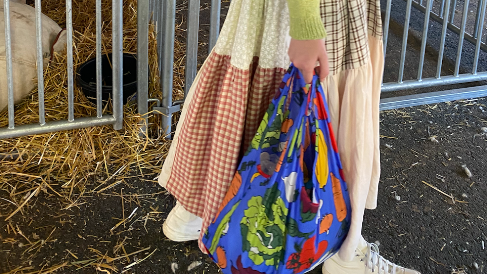 A festivalgoer at New York Sheep and Wool Festival wears a citron green sweater, patchwork frock and veggie print Baggu bag with sneakers.