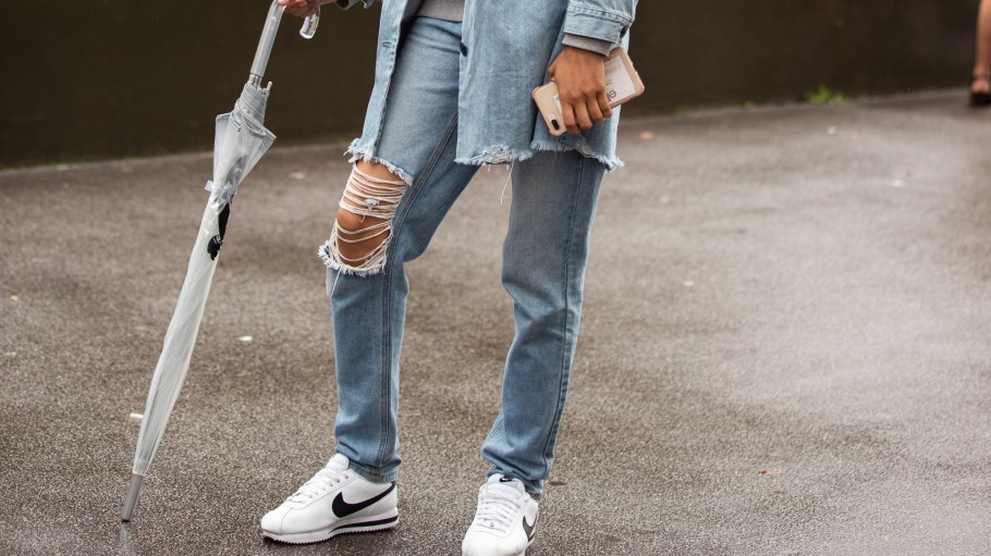 PARIS, FRANCE - SEPTEMBER 25: Model Dahely Nunez wears a denim jacket, gray Tommy Hilfiger sweatshirt, gray Coach bag, blue jeans, white Nike sneakers, and holds a clear umbrella after the Lanvin show during Paris Fashion Week Spring/Summer 2020 on September 25, 2019 in Paris, France.