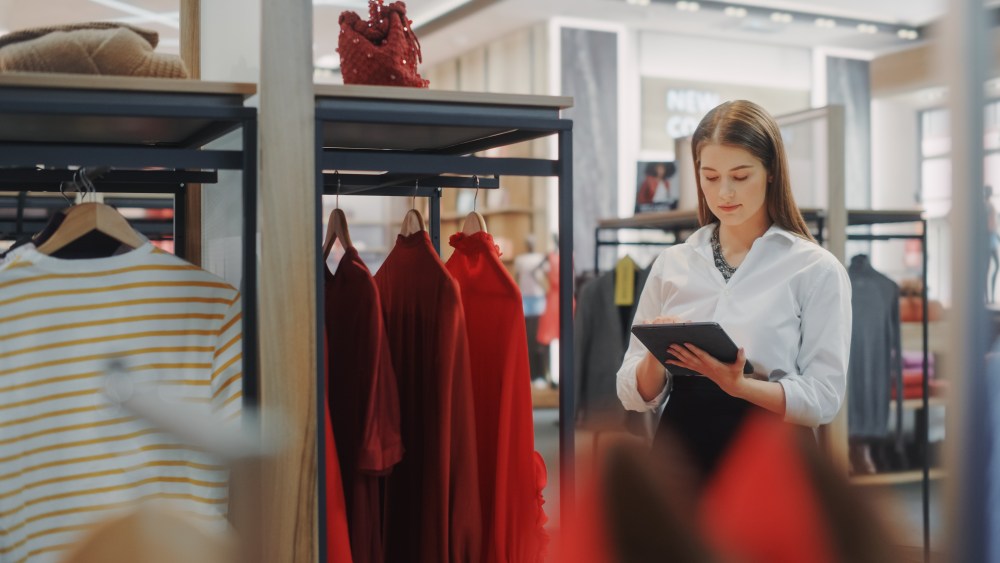 Clothing Store: Female Visual Merchandising Professional Uses Tablet Computer To Create Stylish Collection. Fashionable Shop Sales Retail Assistant Checks Stock. Small Business Owner Orders Items