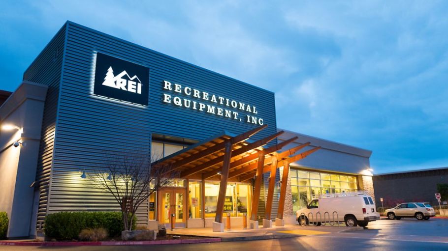 Illuminated facade at dusk with logo and sign at the Recreational Equipment Inc (REI) sports and outdoors equipment store in Dublin, California.