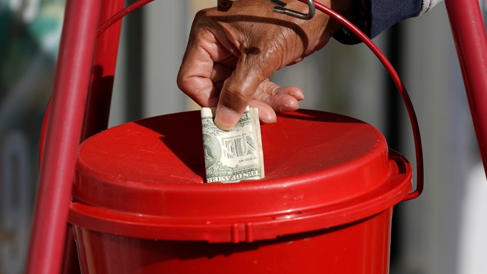 A Corner Market grocery store customer places a dollar in the iconic Salvation Army donations collections bucket in Jackson, Miss., Wednesday, Nov. 25, 2020, as a bell ringer, unseen, wishes customers a "Happy Thanksgiving," while non-vocally soliciting for donations. (AP Photo/Rogelio V. Solis)