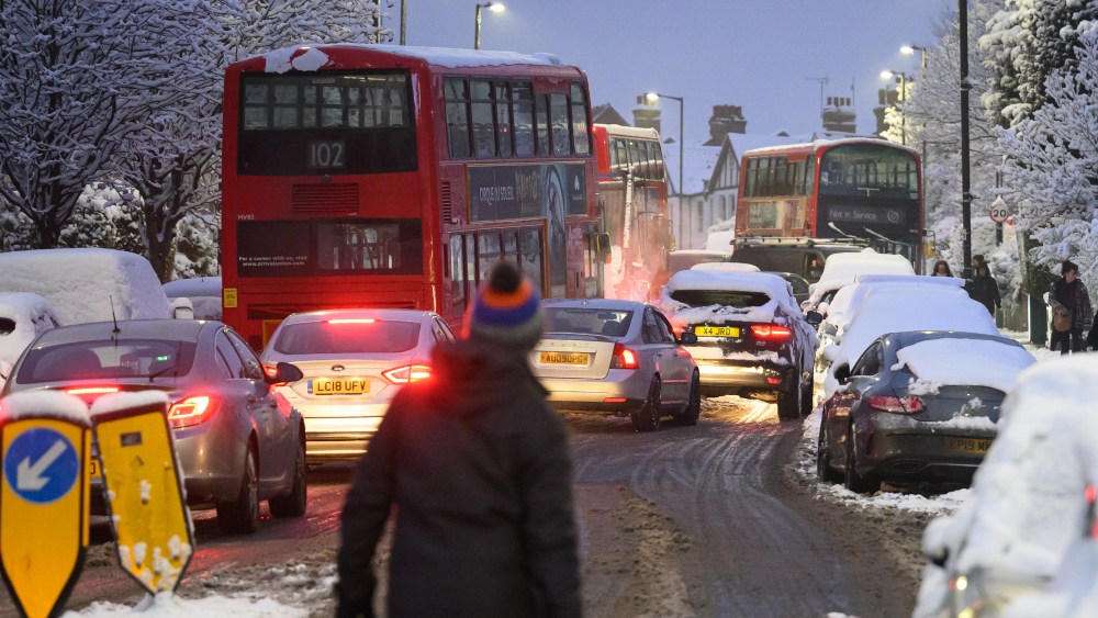 A man walks along an icy road as cars wind around abandoned buses on December 12, 2022 in London, England.
