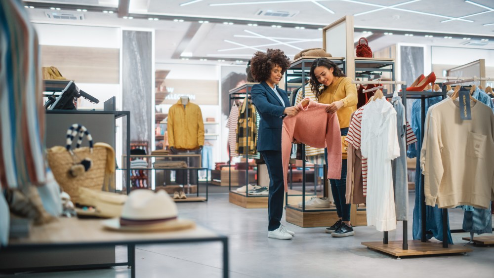 Customers Shopping in Modern Clothing Store, Retail Sales Associate Assists Client. Diverse People in Fashionable Shop, Choosing Stylish Clothes, Colorful Brand Designs, Quality Sustainable Materials.