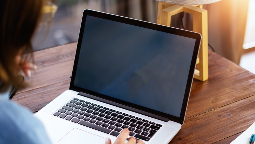 Mockup image of a woman using laptop with blank screen on wooden table. Female writer keyboarding on computer while working on her new article