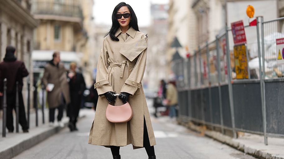 PARIS, FRANCE - MARCH 05: Chriselle Lim wears black sunglasses, a beige linen long belted trench coat, black shiny leather gloves, a pale beige pink shiny leather with silver metallic handle handbag from Lanvin, lack shiny leather pointed heels ankle shoes, black tights , outside Lanvin, during Paris Fashion Week - Womenswear Fall Winter 2023 2024, on March 05, 2023 in Paris, France.