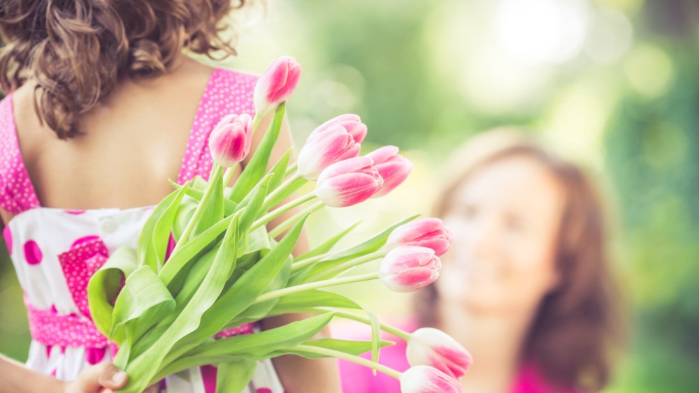 Mother and daughter with bouquet of flowers against green blurred background. Spring family holiday concept. Mother's day