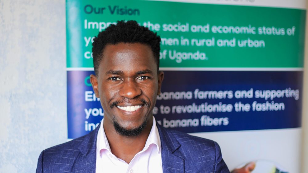 Muhammad “Dimma” Mawejje dressed in blue suiting in front of his business Mawejje Creations