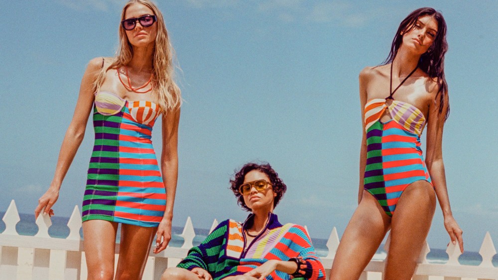 Looks from Staud Sea as worn on three women standing in front of a white picket fence at the beach.