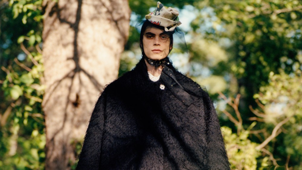 Maison Margiela’s black tactile viscose Neoprene-bonded coat with a bow detail, Ernest Baker’s cotton shirt and Dior wool pants. Rick Owens boots; Maison Margiela Recicla Mickey Mouse cadet hat with a black tulle fascinator.