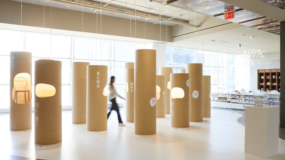 An installation at Muji stores featuring strategically placed paper cylinders and a woman walking between them.