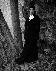 Ferragamo’s wool double natté jacket and cotton shirt and Willy Chavarria’s recycled polyester pleated skirt. Saint Laurent boots; Maison Margiela leather gloves; Thorne Dynasty dagger huggie earring with David Yurman shark tooth amulet in sterling silver with pave black diamonds; Ben-Amun by Isaac Manevitz pearl and crystal necklace; Valentino tie.