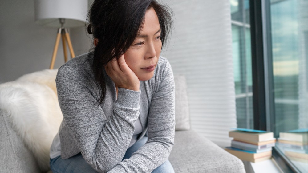 Sad Asian mature woman lonely at home self isolation quarantine for COVID-19 Coronavirus social distancing prevention. Mental health, anxiety depressed thinking senior chinese lady.