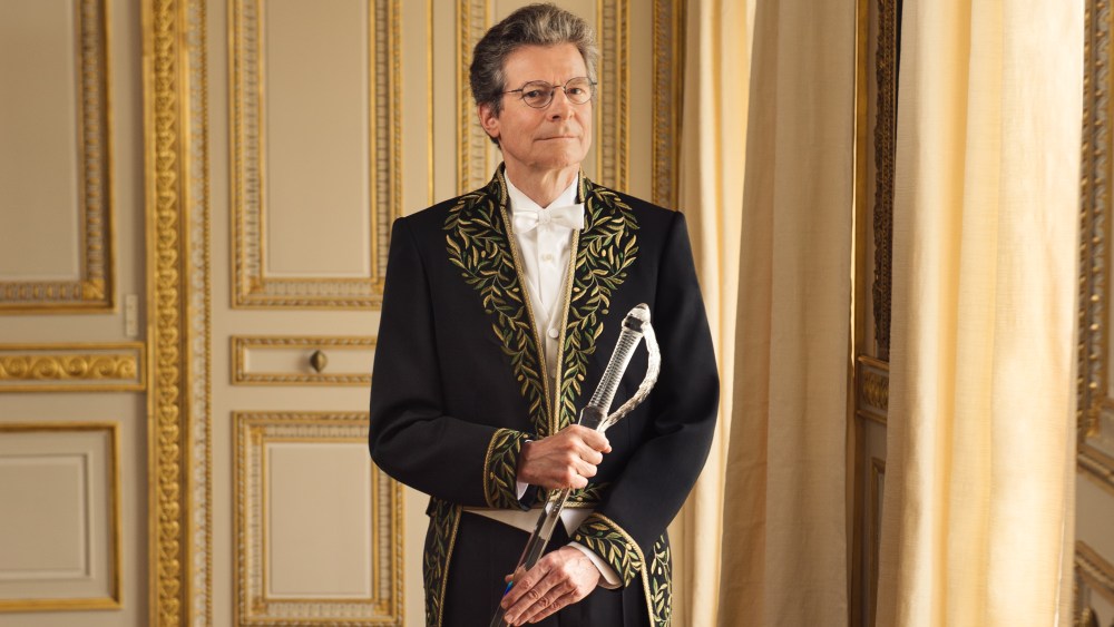 Antoine Compagnon stands in an opulent room with gold molding wearing ceremonial garb by Balenciaga.