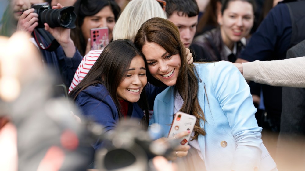 WINDSOR, ENGLAND - MAY 07:  Catherine, Princess of Wales poses for a selfie with a concertgoer during a walkabout meeting members of the public on the Long Walk near Windsor Castle, where the Coronation Concert to celebrate the coronation of King Charles III and Queen Camilla is being held this evening on May 7, 2023 in Windsor, England. The Coronation of Charles III and his wife, Camilla, as King and Queen of the United Kingdom of Great Britain and Northern Ireland, and the other Commonwealth realms took place yesterday at Westminster Abbey today. Charles acceded to the throne on 8 September 2022, upon the death of his mother, Elizabeth II.  (Photo by Andrew Matthews-WPA Pool/Getty Images)