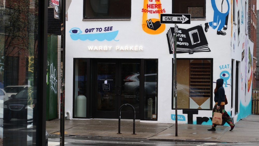Warby Parker store front appearing dark and deserted on a rainy city street. (Photo by Lexie Moreland/WWD/Penske Media via Getty Images)
