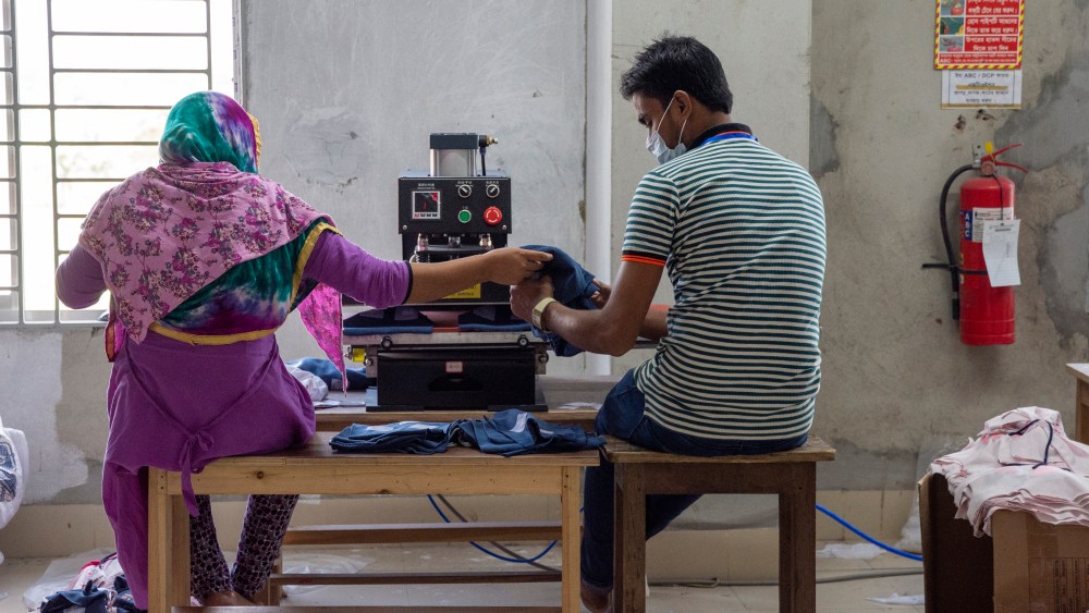 Fair Wear Foundation photograph showcases two garment industry workers, viewed seated from behind a sewing machine sharing the workload.