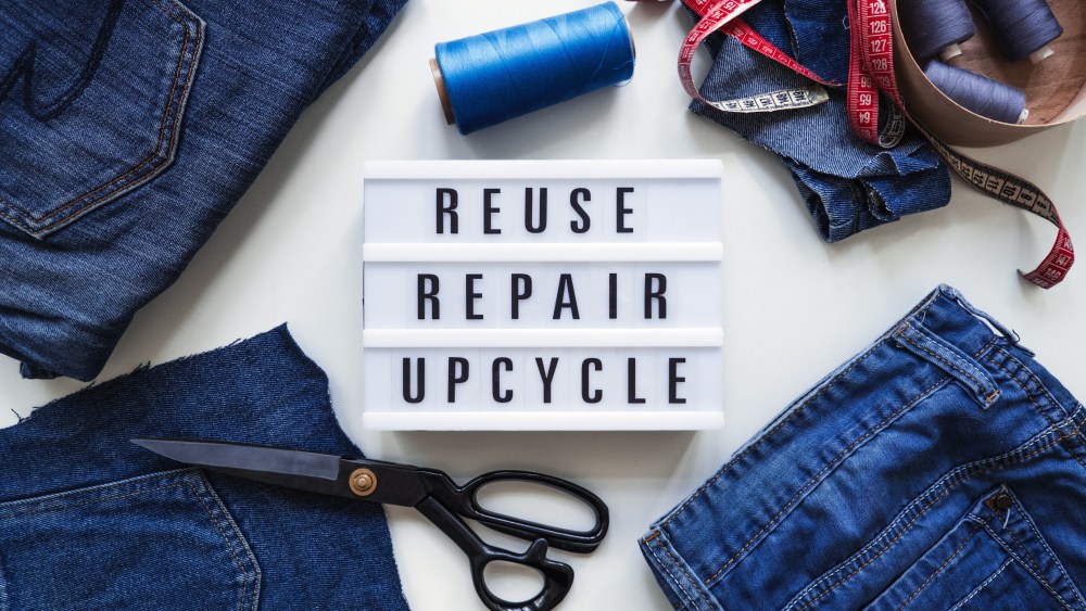 Reuse, repair, upcycle text on light board on sewing machines background. Stack of old jeans, Denim clothes, scissors, thread and sewing tools in sewing studio. Denim Upcycling Ideas, Using Old Jeans.